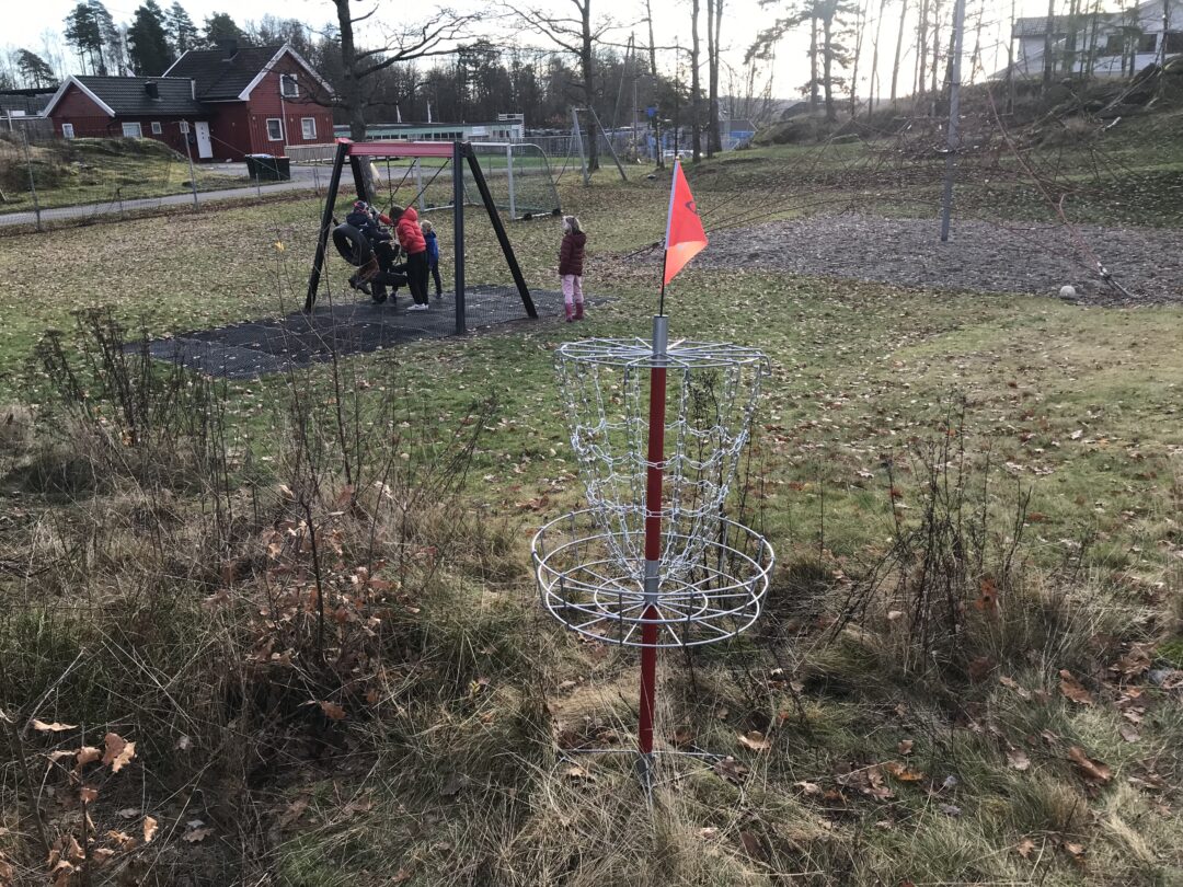 Bilde av frisbeegolf-mål og barn ved huskestativ.