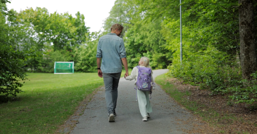 Far som leier barnet sitt på vei til skolen.