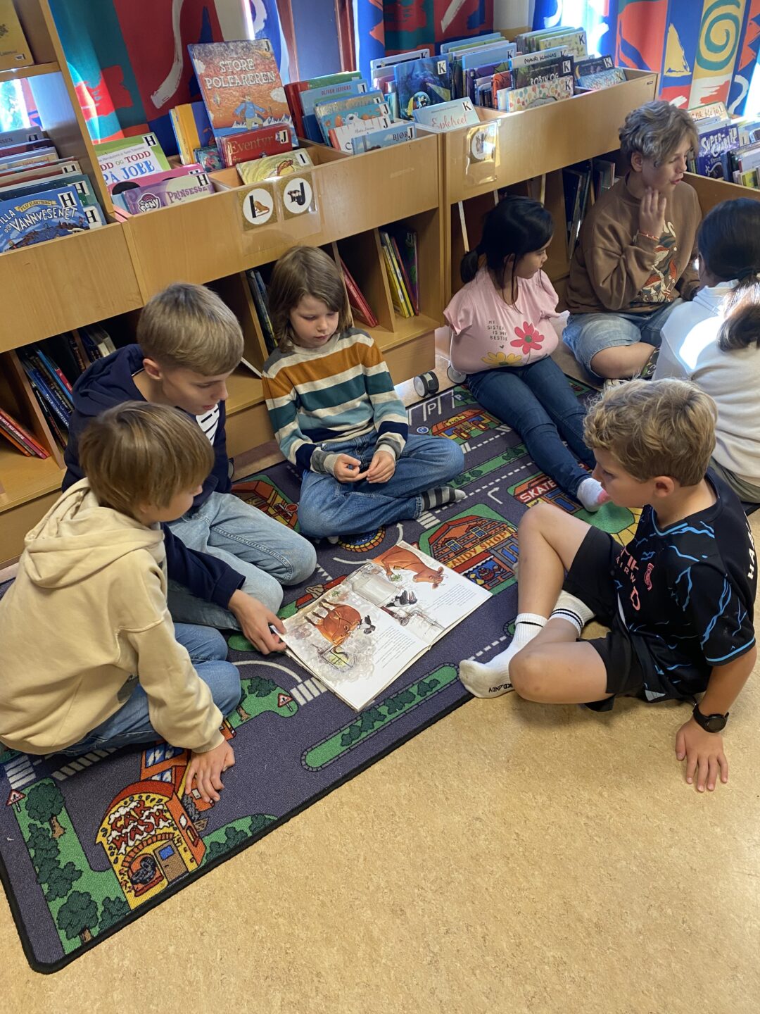 Bilde av elever i 2. og 6. klasse som sitter på gulvet og leser bøker på biblioteket i byen.